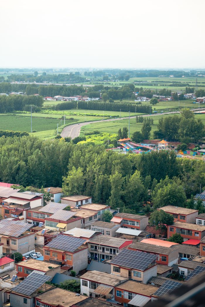 Aerial shot of a rural village surrounded by lush green fields and trees.